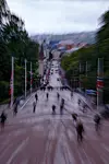 Utsikt ned en bratt gate i Oslo sentrum med folk, flaggstenger og sperringer langs ruten.