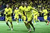 Tre Bodø/Glimt-spillere i gule drakter løper og jubler på fotballbanen foran publikum.