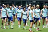 En gruppe norske fotballspillere trener på en gressbane med blå treningsvester og hus i bakgrunnen.