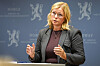 Kjersti Stenseng står ved en talerstol foran en blå bakgrunn med Norge-logoer og snakker med hendene løftet.