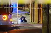 Nattlig gate med avsperring, blått lys og en person som arbeider ved bakken nær et utrykningskjøretøy.