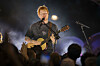 Ed Sheeran står på en opplyst scene med gitar, mens publikum rekker hendene i været foran ham.
