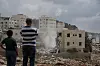 To folk ser på mens en bygning rives i Nablus på Vestbredden, med støv og sammenraste rester.