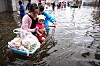 En kvinne og en gutt med en baby står med en handlevogn i vannet. Det er fra flom i Bangkok i Thailand. Foto: AFP/NTB