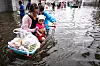 En kvinne og en gutt med en baby står med en handlevogn i vannet. Det er fra flom i Bangkok i Thailand. Foto: AFP/NTB