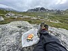 Matpause på en stein på Hardangervidda med fjellsko, turbukse og matpakket inn i DNT-papir.