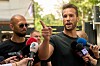 Tristan Tate snakker til mikrofoner mens Andrew Tate står ved siden av utenfor en politistasjon.