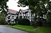 Chi Phi-fraternityhuset ved Cornell University omgitt av trær langs en våt vei.