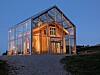 Et opplyst hus med glassfasade står i skumringen på en grusvei.