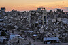 Ruinerte bygninger i Gaza City med mennesker som går langs en vei ved solnedgang.