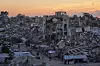 Ruinerte bygninger i Gaza City med mennesker som går langs en vei ved solnedgang.