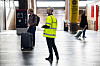Streikevakt i gul refleksvest står i avgangshallen på Oslo S blant reisende og bagasje.