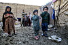 Fire barn står foran et skjul i en steinete leir utenfor Kabul.