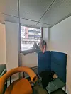Person sitter i en vinduskarm ved blå stoler og en oransje lenestol.
