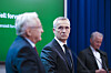 Svein Gjedrem presenterer en rapport for Jens Stoltenberg. De står foran en grønn bakgrunn, og blå gardiner i et presserom.