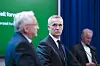 Svein Gjedrem presenterer en rapport for Jens Stoltenberg. De står foran en grønn bakgrunn, og blå gardiner i et presserom.