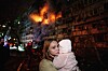 En ung kvinne holder et lite barn foran et brennende, skadet boligbygg i Kyiv.