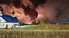 Flammer og mørk røyk stiger bak en hvit kirke med blått tak.