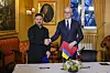 Jonas Gahr Støre og Volodymyr Zelenskyj håndhilser i representasjonsboligen med norske og ukrainske flagg på et bord foran dem i Oslo.