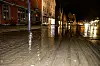 Vann dekker gaten på Bryggen i Bergen om natten, med lysende trehus og speilende overflater.