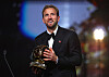 Harry Kane i dress holder Ballon d’Or-statuetten på en opplyst scene.