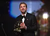 Harry Kane i dress holder Ballon d’Or-statuetten på en opplyst scene.