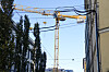 En skjev byggekran ruver mellom bygninger, trær og ledninger mot en klar blå himmel i Oslo sentrum.