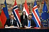 Espen Barth Eide og Andras Karman signerer avtaler foran norske, ungarske og europeiske flagg.