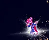 Fargerik rosa og blå figur omgitt av stråler og glitrende lys mot mørk bakgrunn.