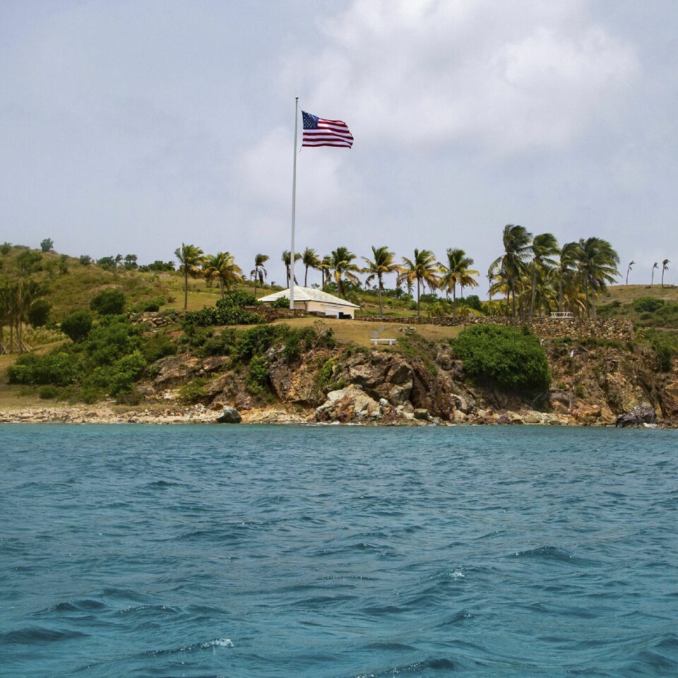 OVERGREPSDØMT: Jeffrey Epstein ble dømt for overgrep. Her er øya han eide. Den heter Little St. James Island. Flere av overgrepene skal ha skjedd her. Øya ble kalt «pedofiløya» av lokale. Bildet er av øya Little St. James. Bildet er tatt fra havet. Det amerikanske flagget vaier høyt midt på øya, med et lite hus rett under seg.