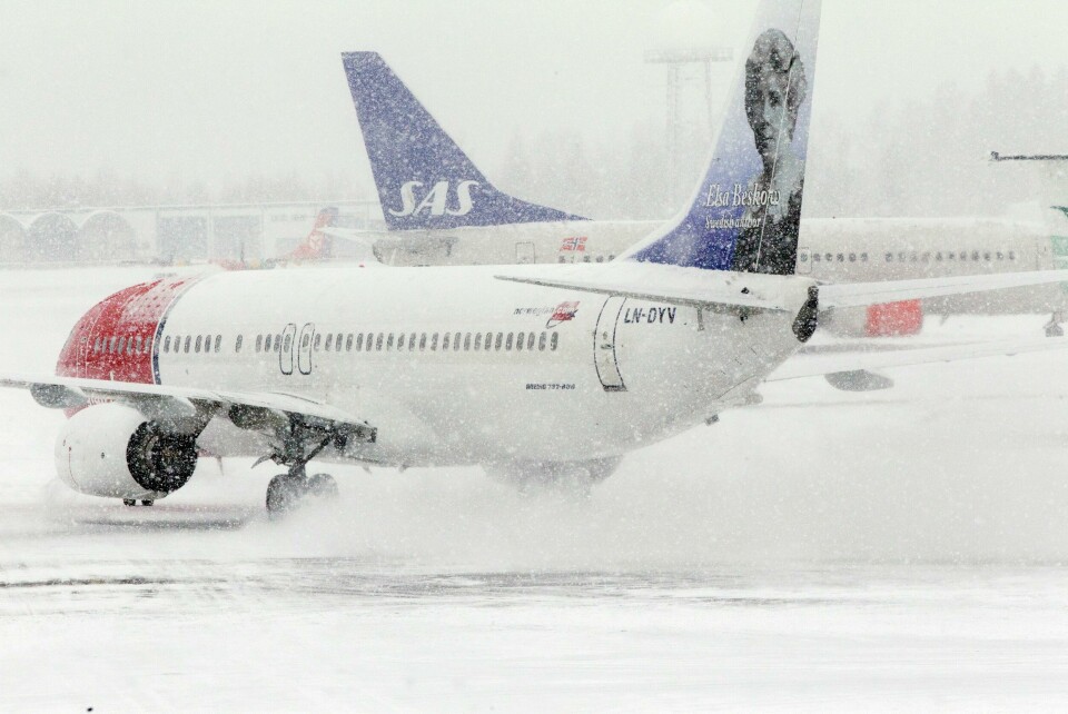 EKSTRA: Det skal bli flere avganger og ruter til jul. Slik skal selskapene frakte flest mulig hjem til jul. Vukdet er av et fly fra Norwegian som lander i snøvær på Oslo Lufthavn. Det står et fly fra SAS i bakgrunnen.
