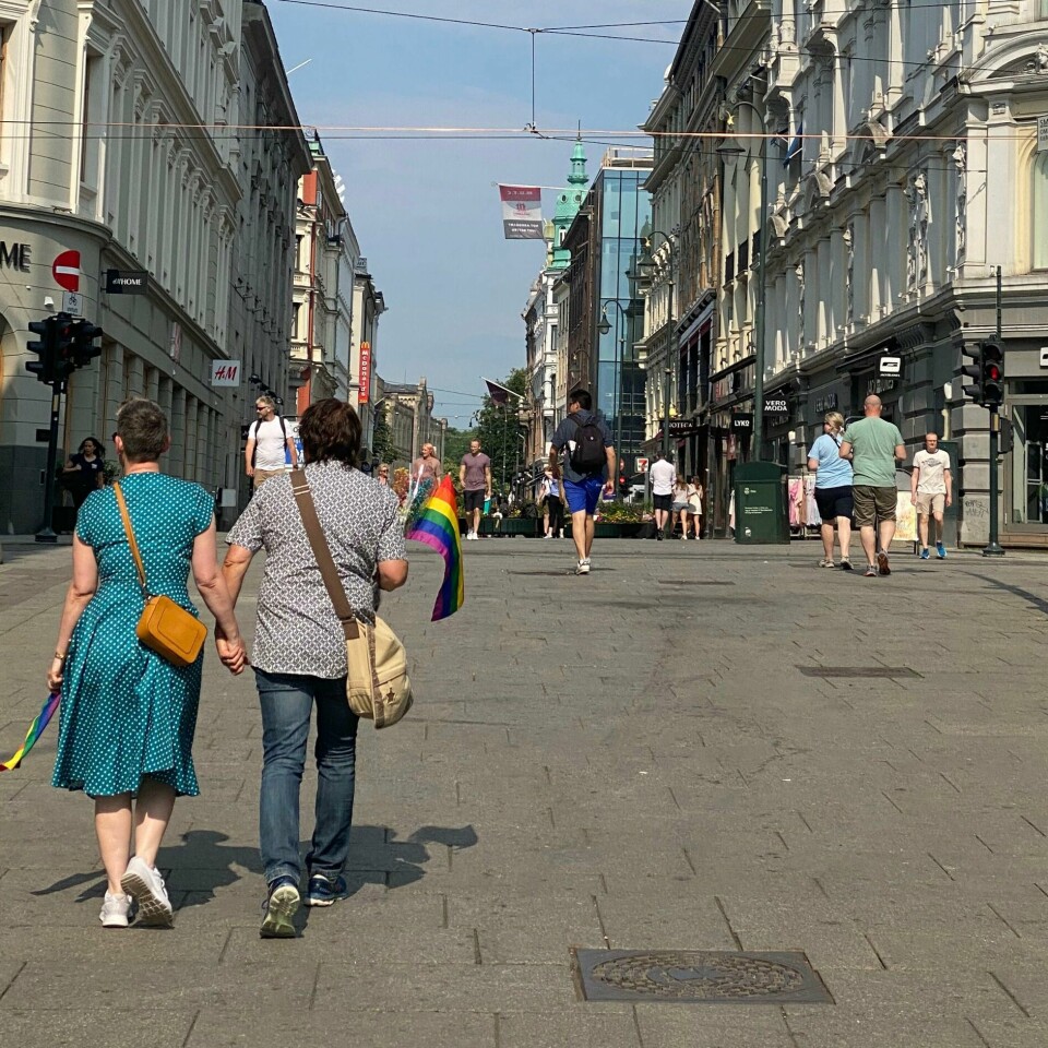 PAR: Et par med regnbueflagg og blomster går sammen på Karl Johans gate i juni i fjor. De skulle vise sin omtanke etter skytingen i Oslo under pride. Støtte fra oss alle og sikkerhet er viktig for at skeiv kjærlighet får være trygg. Bildet viser et par med to kvinner som holder hender. De har regnbueflagg og blomster.