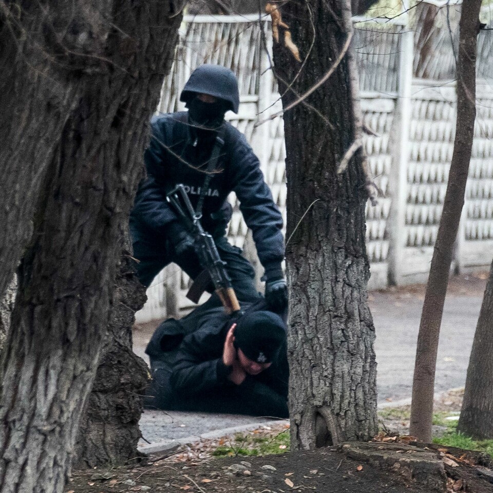 VOLD: Det har vært mye vold som følge av protestene i Kasakhstan. Minst 164 personer er drept. Nesten 8.000 er pågrepet. Bildet er av en væpnet politimann med maske og hjelm som sikter et automatvåpen i nakken på en demonstrant som ligger på bakken med ansiktet ned. Det er mulig å se dem mellom noen trær. Foto: Vasily Krestyaninov / AFP / NTB
