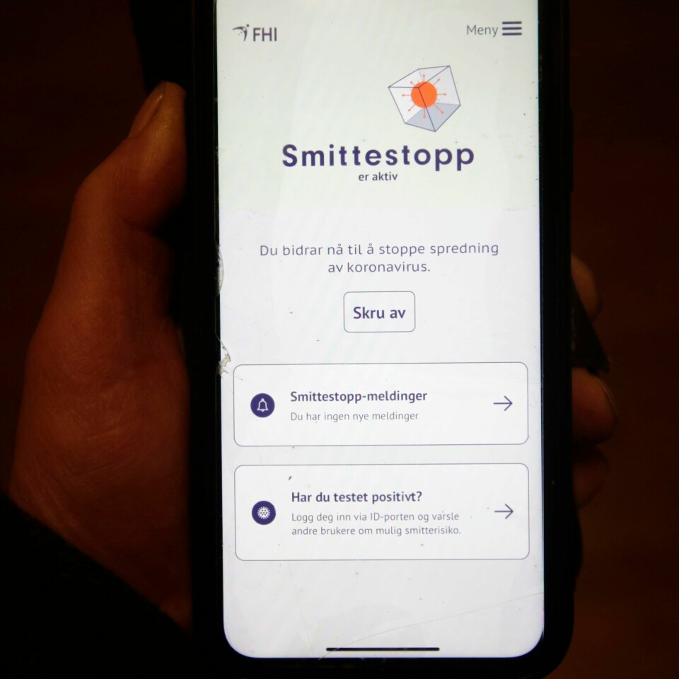 RASKT: Korona smitter nå så raskt at appen Smittestopp sliter med å holde følge. Det gjør at den har lite nytte nå, ifølge eksperter. Bildet er av en hånd som holder en mobiltelefon i et mørkt rom. På skjermen er det mulig å se forsiden på appen Smittestopp. Foto: Terje Bendiksby / NTB