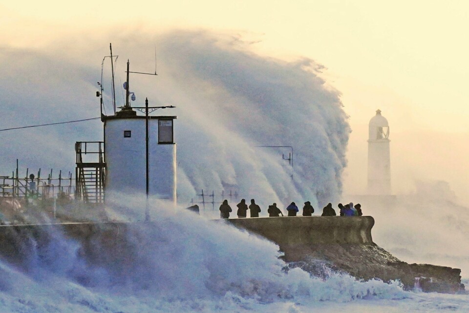 STORM: Store bølger treffer et fyrtårn i Wales i Storbritannia. Stormen Eunice herjer. Bildet viser store bølger som fosser over et fyrtårn i Wales. Folk står rundt og ser på.