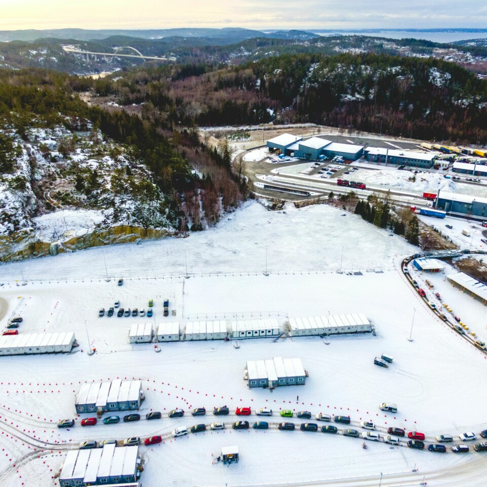 KØ: Det har til tider vært lange køer for å teste seg på Svinesund. Slik var det også i desember da det ble strenge regler for å bremse omikron. Bildet er av lange køer med biler på teststasjonen på Svinesund i desember. Det er snø på bakken, og bildet er tatt fra høyt oppe i lufta. Det står brakker rundt omkring på et stort område, hvor bilister kjører inn for å teste seg. Foto: Stian Lysberg Solum / NTB