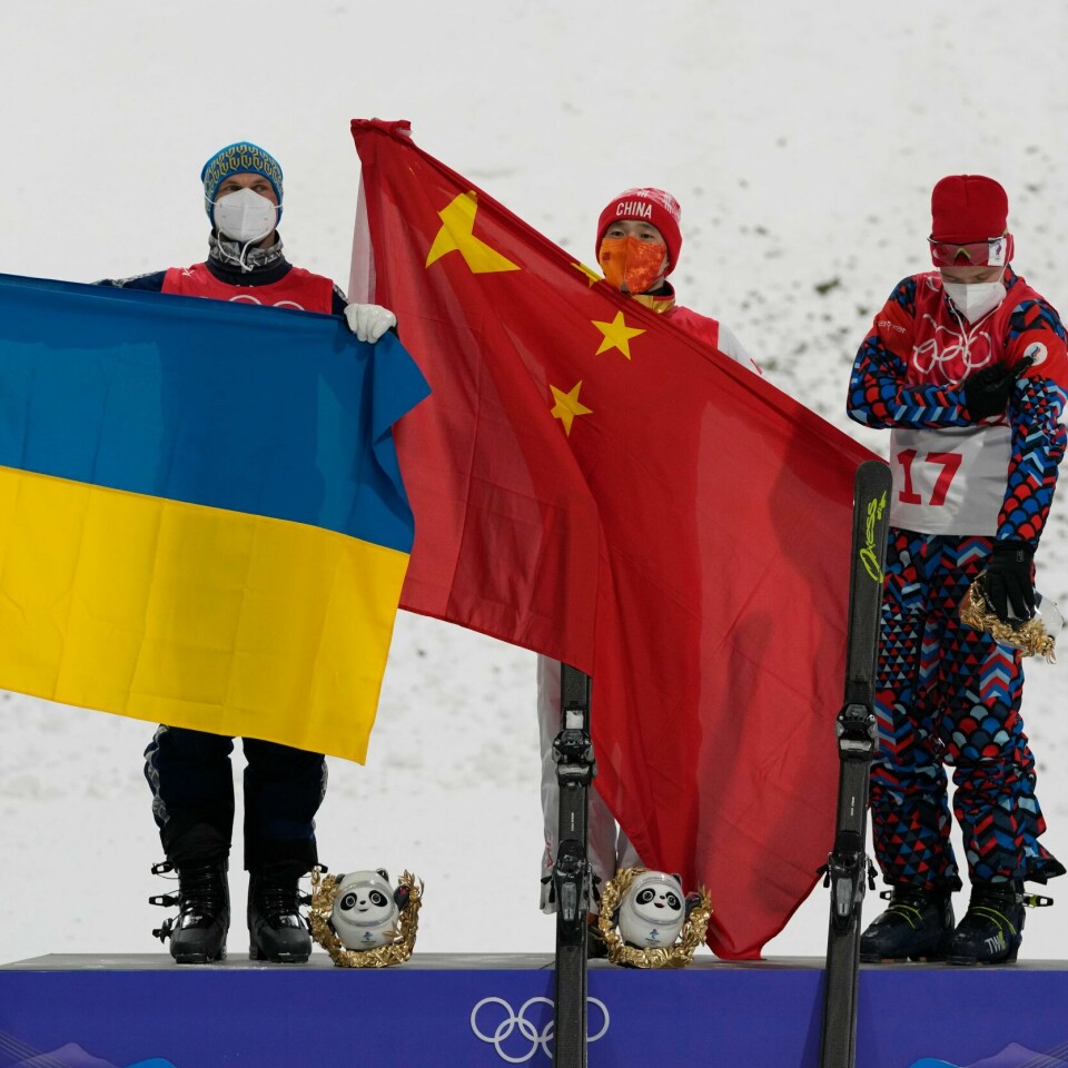 VANT: Qi Guangpu vant OL-gull. Han feiret med flagget til Kina. Oleksander Abramenko feiret sølv med sitt ukrainske. Russiske Ilja Burov vant bronse, men måtte klare seg uten flagg. Bildet er av Qi Guangpu med kinesisk og Oleksander Abramenko med ukrainsk flagg på seierspallen etter fristilhoppernes OL-finale. Russeren Ilja Burov på bronseplass må greie seg uten flagg. Foto: Lee Jin-man, AP / NTB