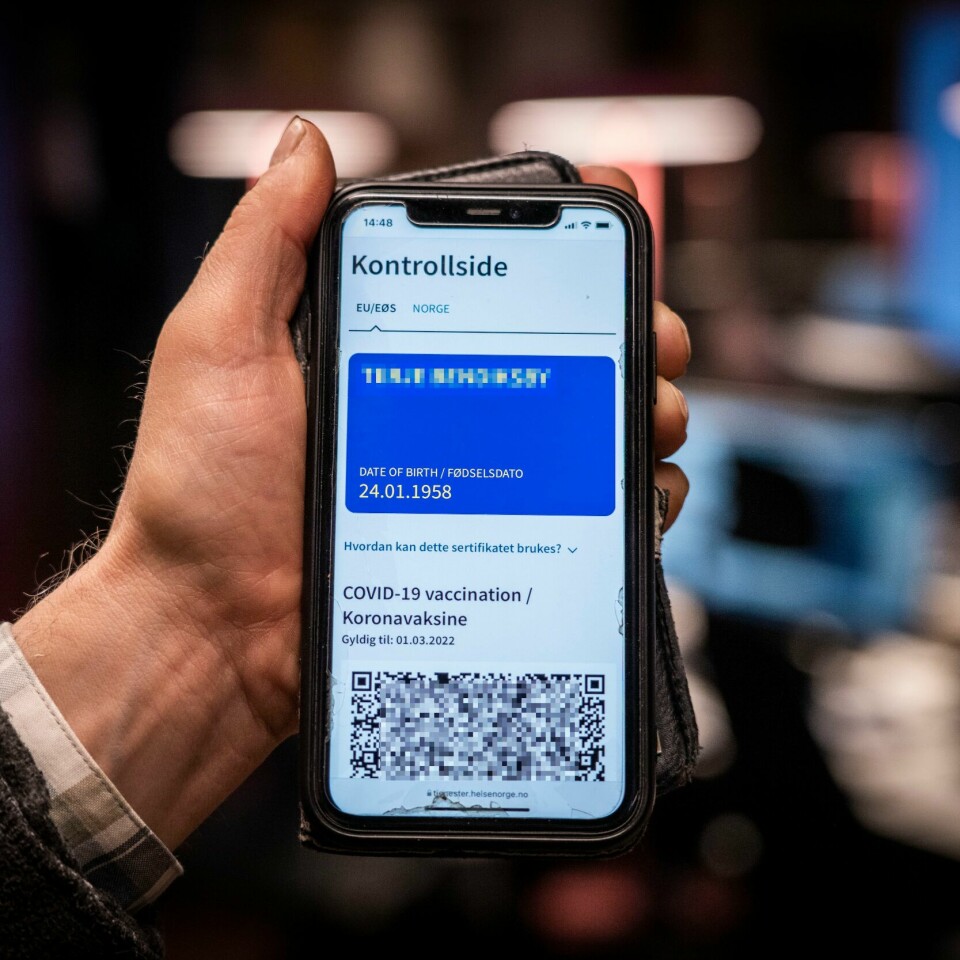 LENGER: Du kan bli nødt til å vise den blå siden i koronapasset fram til neste sommer. Bildet er av en hånd som holder opp en mobil. Skjermen viser et blått koronapass. Foto: Ole Berg-Rusten / NTB
