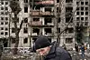 Bildet viser en eldre mann i Kyiv. I bakgrunnen ser vi en ødelagt boligblokk.