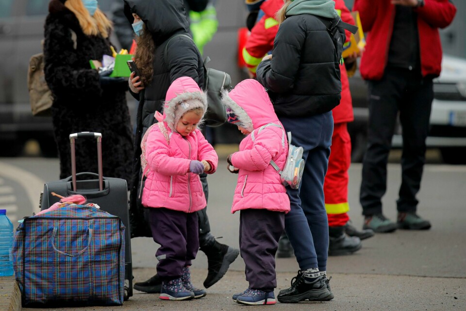 FLYKTET: To barn som har flyktet fra Ukraina, åpner godteri. Det har de har fått fra frivillige på grensa til Romania. Bildet viser to barn i like, rosa jakker som har flyktet fra Ukraina. De to åpner godteri som de har fått fra frivillige på grensa til Romania.