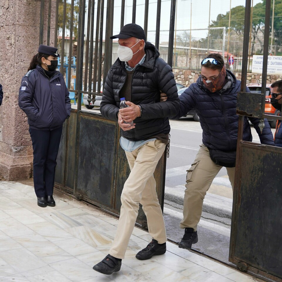 SIKTET: Norske Knut Bry er siktet for spionasje i Hellas. Bildet er av en eldre mann som blir fulgt inn en stor jernport. Han blir holdt av en politimann, mens det står andre politifolk og ser på. Mannen er den norske fotografen Knut Bry. Foto: Panagiotis Balaskas / AP / NTB