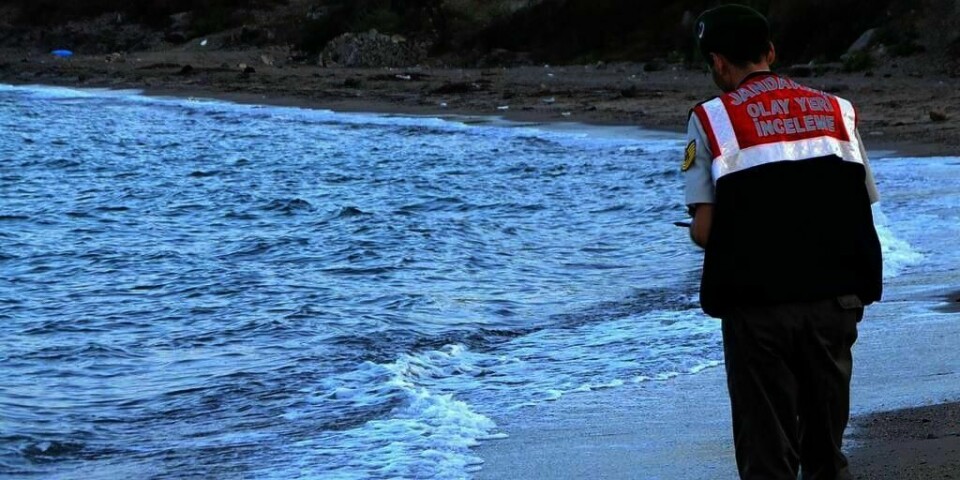 Trist: En tyrkisk tjenestemann på stranden i Bodrum i Tyrkia. Like ved ham ligger en liten gutt som har blitt skylt i land. Han har druknet. Klar Tale har valgt å ikke vise bildet av gutten.