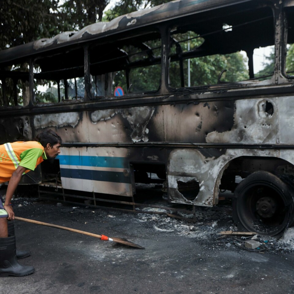 ADVARER: Som følge av protester og vold mener UD at nordmenn bør unngå reiser til Sri Lanka. Bildet er av en mann som lener seg framover og tar seg til knærne. Han ser på restene av en utbrent buss. Foto: Dinuka Liyanawatte / Reuters / NTB