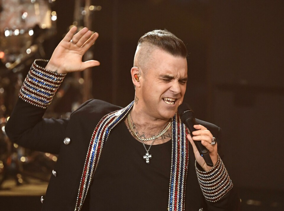 DRØM: Robbie Williams har en drøm om å få synge i Eurovision-finalen neste år. Bildet viser Robbie Williams som synger. Han har en svart genser. Han holder en mikrofon i en hånd og holder den andre i været. Det er et juletre i bakgrunnen. Foto: AP