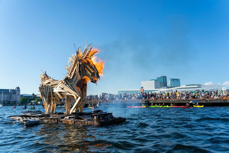 BÅL: Slik så det ut på Sukkerbiten i Oslo for ett år siden. Det var Ordfører Marianne Borgen som tente på hesten. Dette året blir det en ny skapning som skal være bål. En hest står på vannet. Hesten er bygget med treverk og er blitt tent på. Flammene er kun på hodet til hesten foreløpig, men dette skal bli et stort sankthansbål og hele hesten skal bli påtent. Folk står rundt å ser på det store bålet.