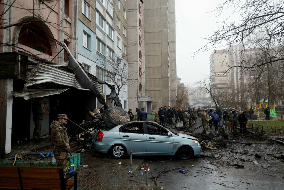 KRASJ: Et helikopter krasjet i en bydel av Kyiv onsdag morgen. Flere personer skal ha dødd. Bildet er av folk som står rundt en bil. Den er parkert foran et bygg som er skadd etter at helikopter krasjet. Foto: Valentyn Ogirenko / Reuters / NTB