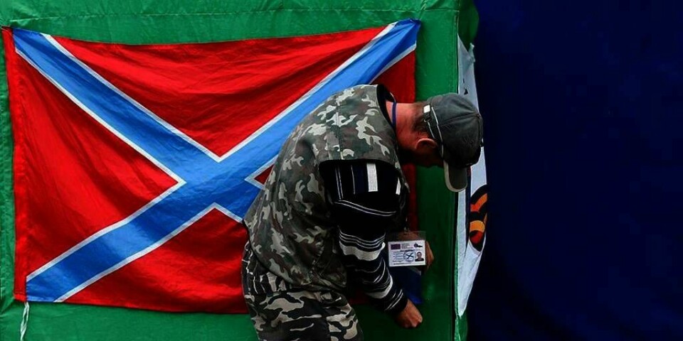 STYRE: Folk i Øst-Ukraina skal få bestemme over flere ting selv. Dette bestemte nasjonal-forsamlingen tirsdag. Mannen på bildet er en opprører som støtter Russland. Han henger opp et flagg som skal vise at området ved byen Donetsk er en egen stat.