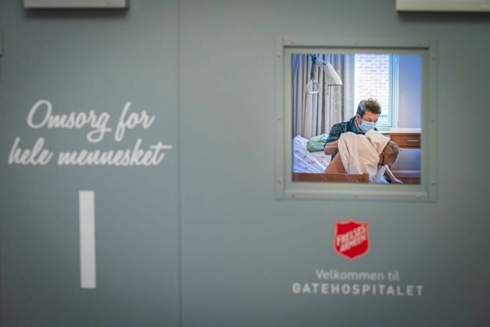 STENGER: Rusavhengige og hjemløse rammes hardt av koronakrisen. Flere av tilbudene er nødt til å stenge. Bildet viser en dør på Gatehospitalet til Frelsesarmeen. Gjennom et vindu i døren kan du se en lege som undersøker en rusavhengig.