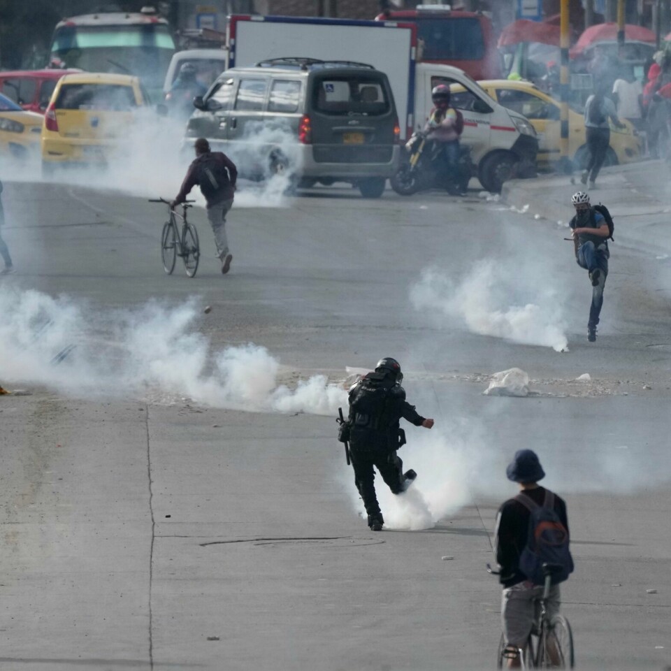 PROTEST: En politimann og en demonstrant sparker granater med tåregass mot hverandre i Bogotá. Mandag var det nye sammenstøt mellom politi og demonstranter i byen. En politimann og en demonstrant sparker tåregassgranater mot hverandre i Bogota. Mandag var det nye sammenstøt mellom politi og demonstranter i byen. Foto: Fernando Vergara / AP / NTB