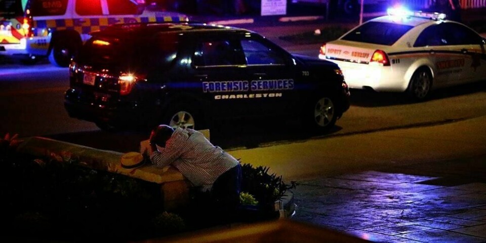 KNELER: En mann kneler ned utenfor en kirke i Charleston i USA. En hvit mann kom inn i kirken og skjøt rundt seg. Ni mennesker ble drept.